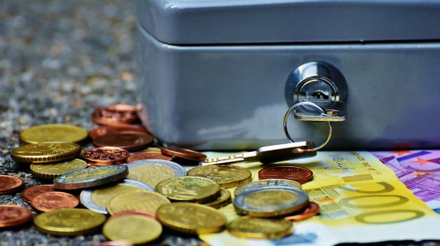 Gespartes Geld, welches vor einer zugeschlossenen Kasse liegt