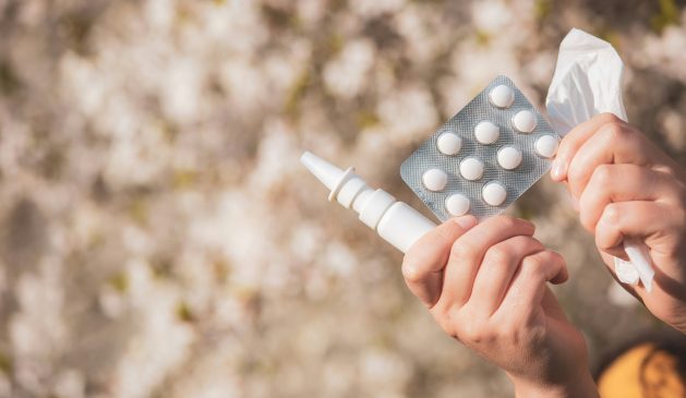 Eine Person hält ein Nasenspray, ein Blister mit Tabletten und ein Taschentuch