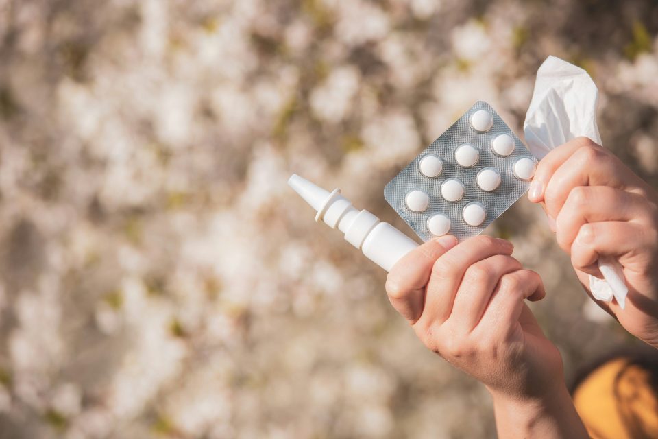 Eine Person hält ein Nasenspray, ein Blister mit Tabletten und ein Taschentuch