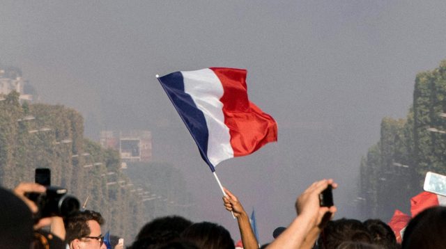 Eine Person in einer Menschenmenge, welche die Frankfreichflagge in der Hand hält