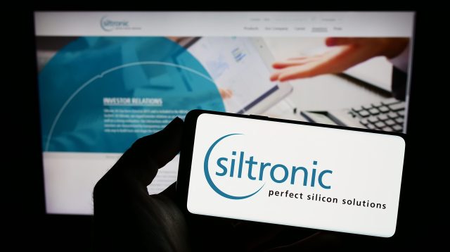 Person hält Smartphone mit Logo des deutschen Elektronikunternehmens Siltronic AG auf dem Bildschirm vor einer Website mit Fokus auf das Telefondisplay