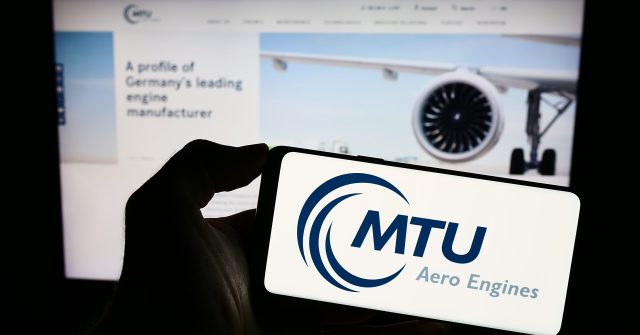 Eine Person hält ein Smartphone mit dem Logo des deutschen Luftfahrtunternehmens MTU Aero Engines AG auf dem Bildschirm vor einer Website