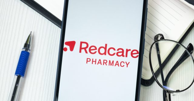 Redcare Pharmacy Logo auf dem Handy am Schreibtisch