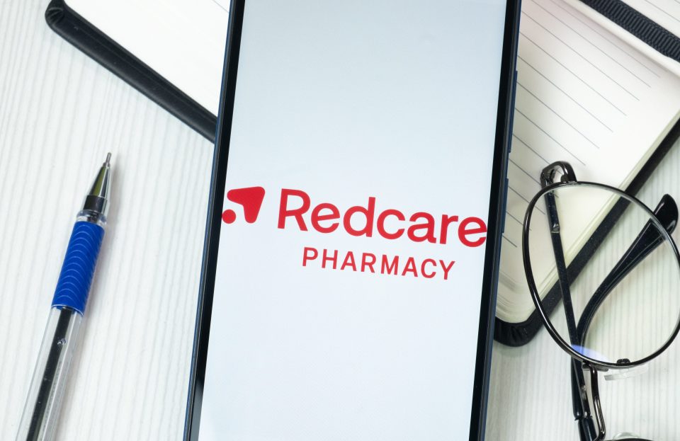 Redcare Pharmacy Logo auf einem Handy am Schreibtisch