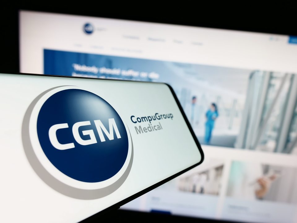 Ein Mobiltelefon mit Logo der Firma CompuGroup Medical SE Co. KGaA (CGM) auf dem Bildschirm vor einer Website mit Fokus auf die Mitte links des Telefondisplays