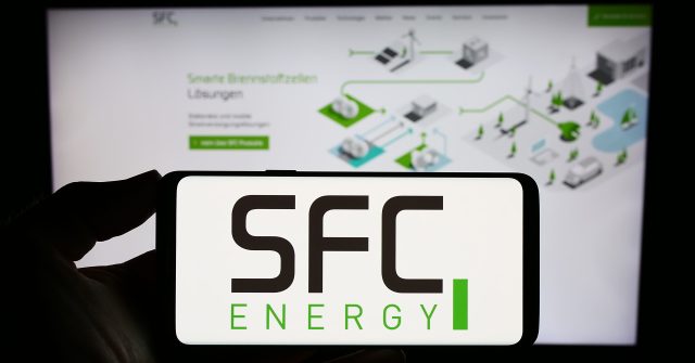 Eine Person hält ein Smartphone mit dem Logo des deutschen Unternehmens SFC Energy AG auf dem Bildschirm vor einer Website mit Fokus auf das Telefondisplay