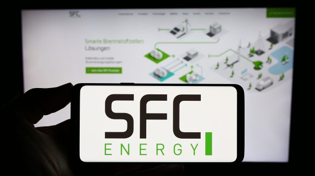 Eine Person hält ein Smartphone mit dem Logo des deutschen Unternehmens SFC Energy AG auf dem Bildschirm vor einer Website mit Fokus auf das Telefondisplay