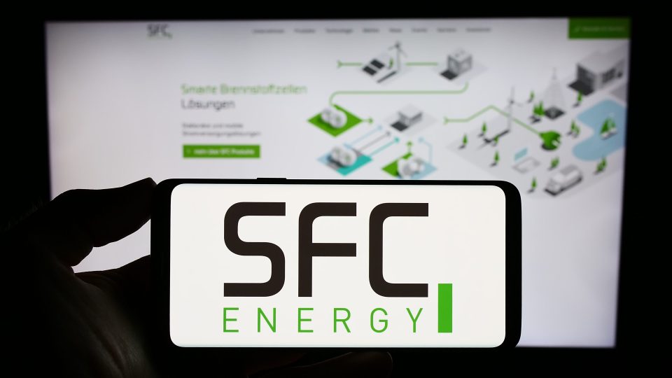 Eine Person hält ein Smartphone mit dem Logo des deutschen Unternehmens SFC Energy AG auf dem Bildschirm vor einer Website mit Fokus auf das Telefondisplay